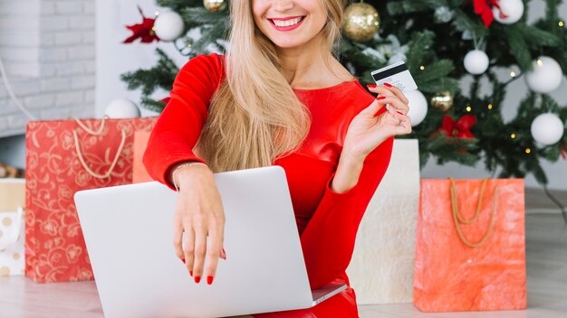Woman sitting with laptop and card near Christmas tree