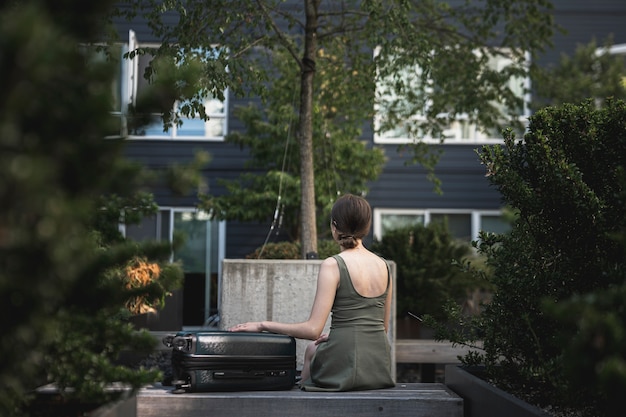 Foto gratuita donna che si siede con una valigia nel parco
