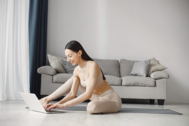 Woman sitting on yoga man in leggins and top while using on laptop at home