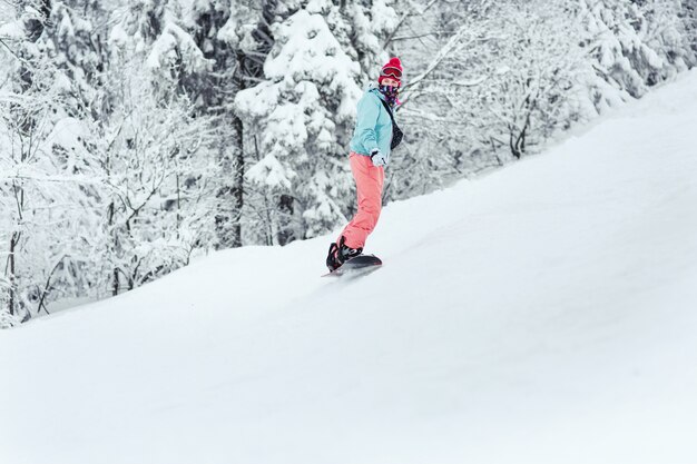 彼女のスノーボードの丘の下を行く彼女の肩の上にスキースーツの女が見える