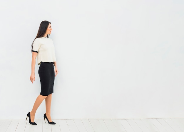 Woman in skirt suit standing on white wall background 