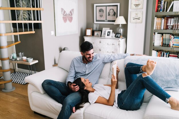 Woman sleeping on man's lap showing her book at home