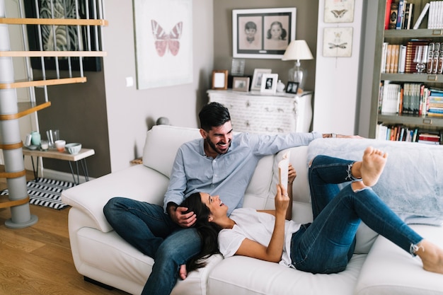 Woman sleeping on man's lap showing her book at home