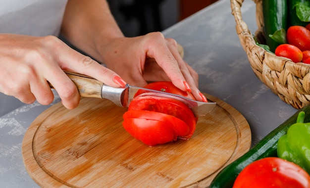 灰色の表面にまな板のハイアングルでトマトをスライスする女性