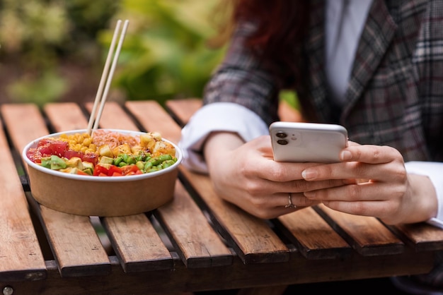 A woman in smartphone and poke bowl in a park