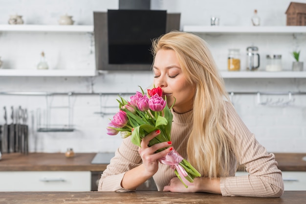 Женщина пахнущие свежие цветы на кухне