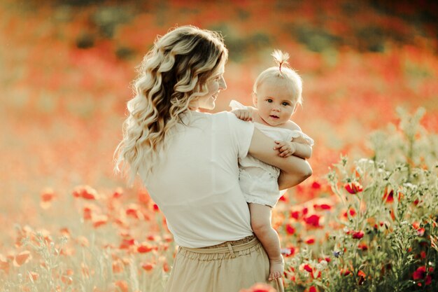 Woman smiles to a baby among flower field