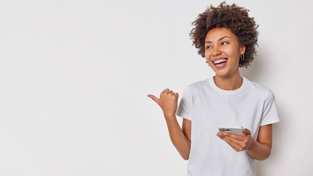 Женщина улыбается, широко держит мобильный телефон, отправляет текстовое сообщение, указывает большой палец на левую сторону для копирования вашего рекламного контента. концепция рекламы технологии людей
