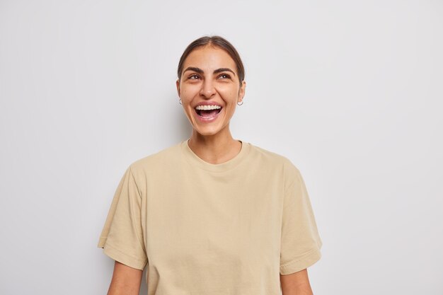 woman smiles gladfully has upbeat mood laughs at something dressed in casual beige t shirt on white