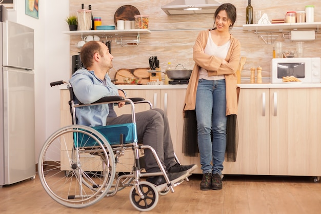 Woman smiling at disabled husband in wheelchair while talking with him. Disabled paralyzed handicapped man with walking disability integrating after an accident.