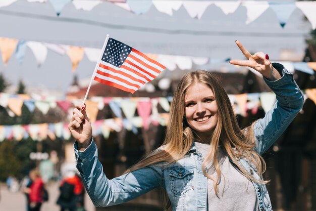 Woman smiling holding American flag and gesturing two fingers 