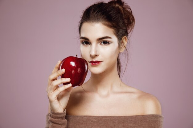 woman smiling holding red apple on pink