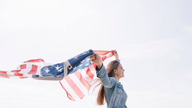 Woman smiling and holding wide waving  American flag high in sky