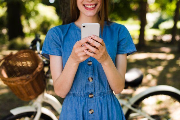 Женщина улыбается на телефон с расфокусированным велосипед