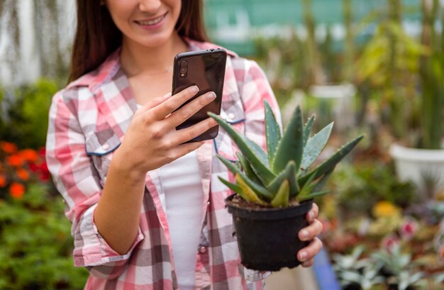 Woman smiling taking picture of plant with phone in greenhouse