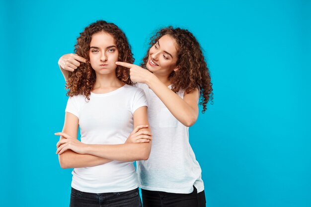 woman smiling, touching cheeks her sister twin over blue.
