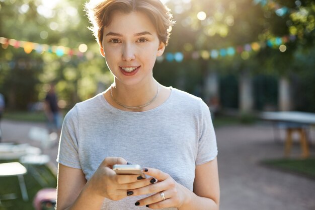 スマートフォンを使用して笑っている女性。笑顔と屋外で彼女の携帯電話を使用して若い幸せな女性の肖像画