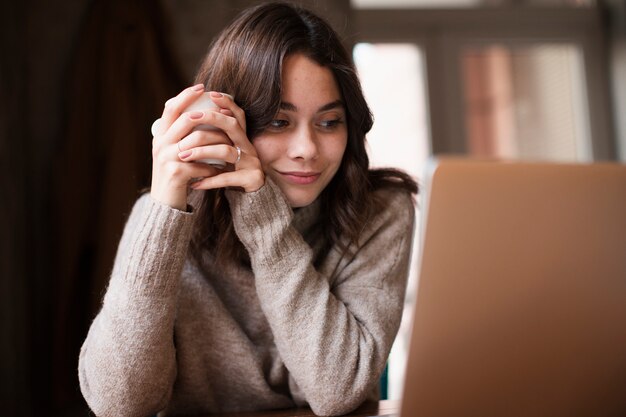 Woman smiling while holding cup and looking at laptop