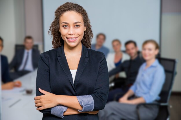 Woman smiling with arms crossed and colleagues out of focus