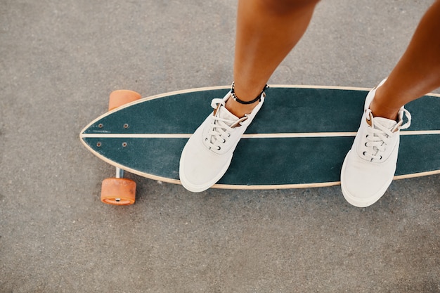 아스팔트 표면에 야외 스케이트 보드를 타고 운동 화에 여자.