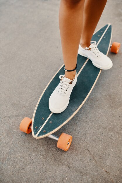 Woman in sneakers riding skateboard outdoor on asphalt surface.