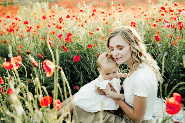 Woman snuggles to her baby on the poppy field