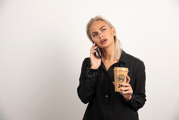 Женщина разговаривает по мобильному телефону и держит чашку кофе. Фото высокого качества