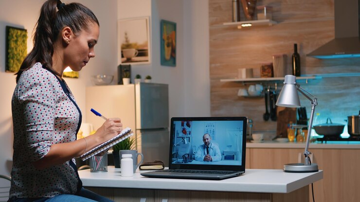 Free Photo woman speaking online with doctor taking notes during tele health sitting in home kitchen. sick lady discussing during virtual consultation about symptoms holding notebook and writing treatment