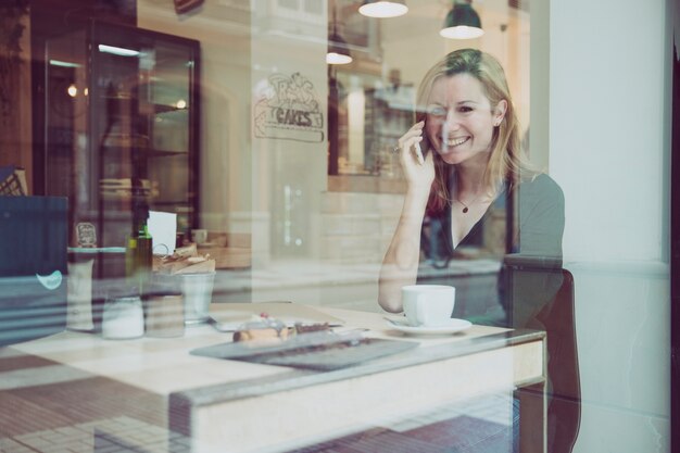 Woman speaking on phone and looking at camera in cafe