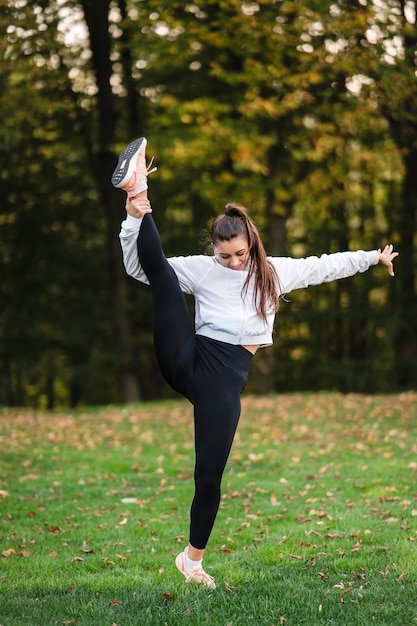 公園でスポーツ服を着た女性が立ってスプリットをしています。