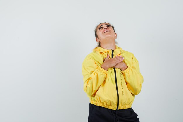 Woman in sport suit holding hands on chest and looking hopeful , front view.