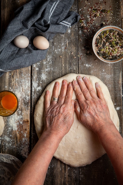 Woman spreading dough with hands on wooden table top view.