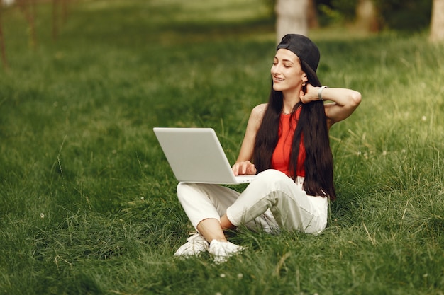 Woman in a spring city. Lady with a laptop. Girl sitting on a grass.