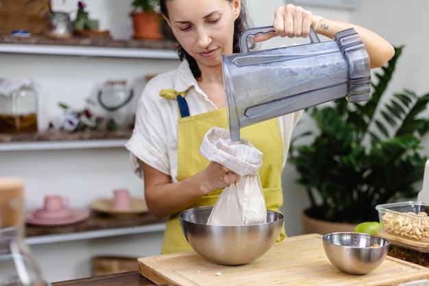 Бесплатное фото Женщина выжимает миндальное молоко из миндаля на кухне дома