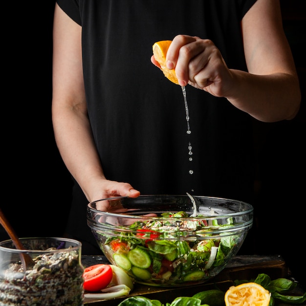 Woman squeezing lemon into chunky salad side view.