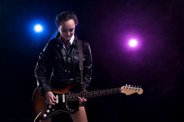 Woman on stage with lights playing the guitar