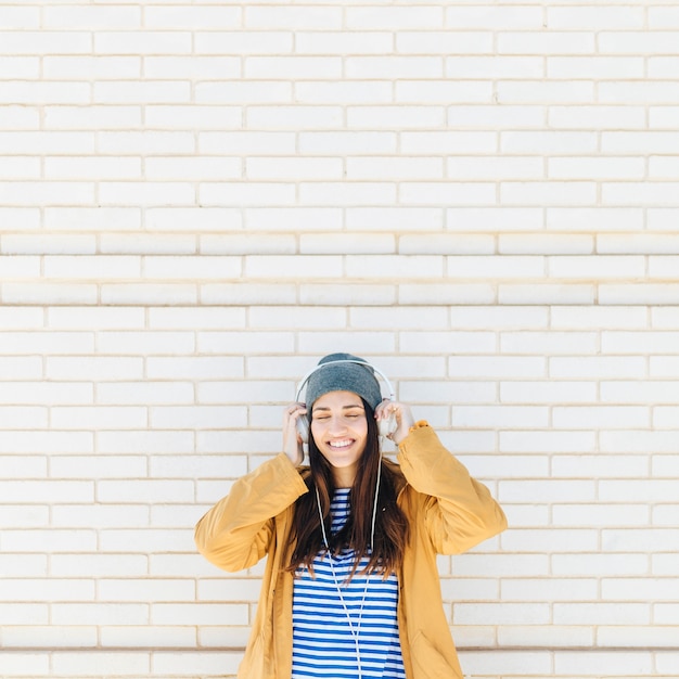 woman standing against brick wall enjoying listening music with her eyes closed