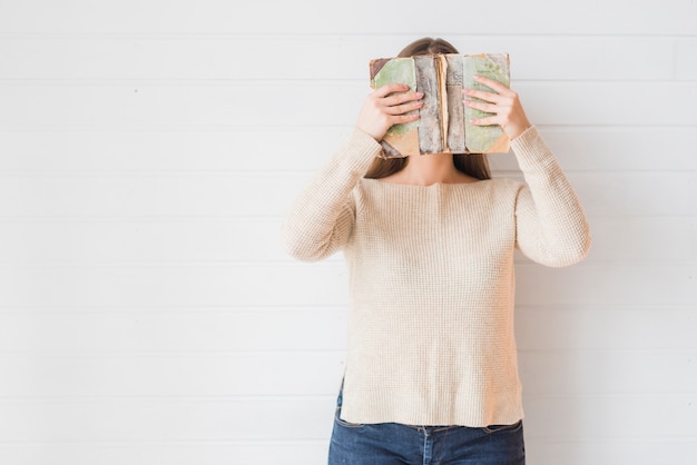 Free photo woman standing against wall covering her face with book