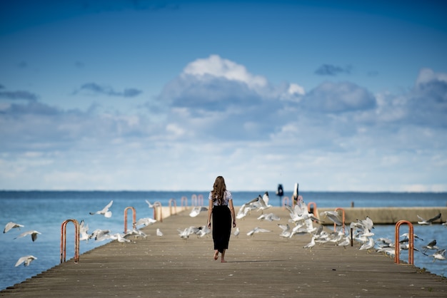 Free photo woman standing on a boardwalk surrounded by birds