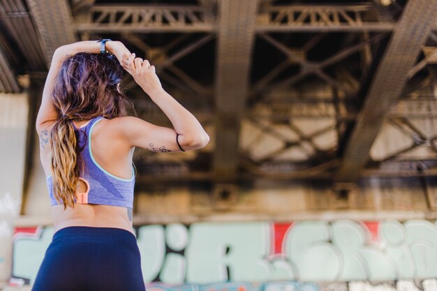 Free photo woman standing under bridge stretching arms