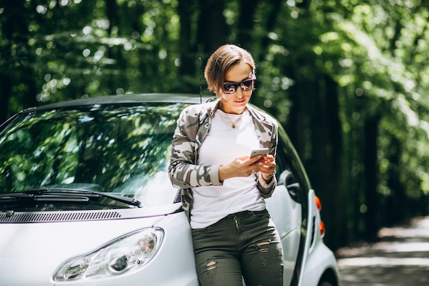 Женщина, стоя у машины в парке с помощью телефона