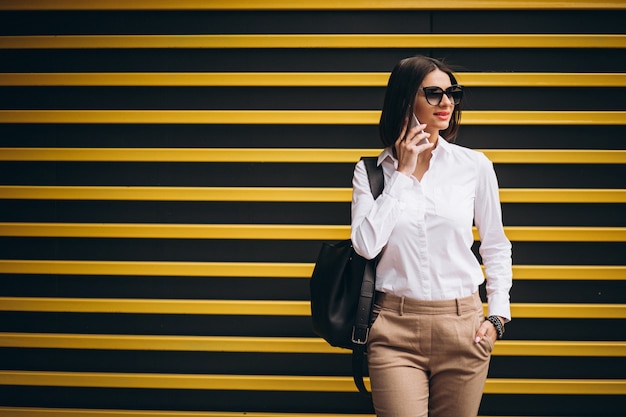 Woman standing by the yellow wall and talking on the phone