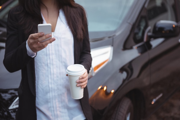 Woman standing next to a car and using mobile phone