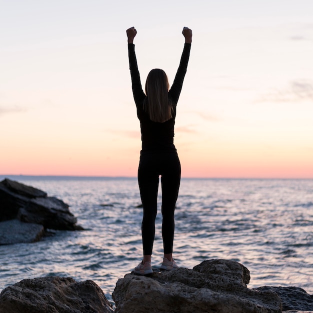 Woman standing on a coast with her arms up