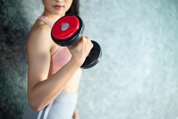 Woman standing exercising with a red dumbbell in the gym.