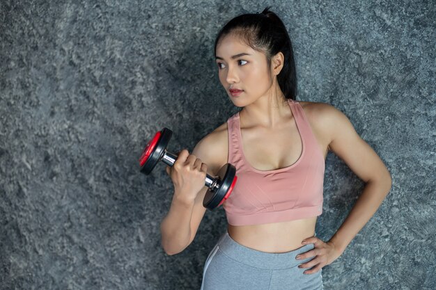 Woman standing exercising with a red dumbbell in the gym.