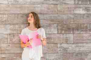 Free photo woman standing in front of wall holding pink book