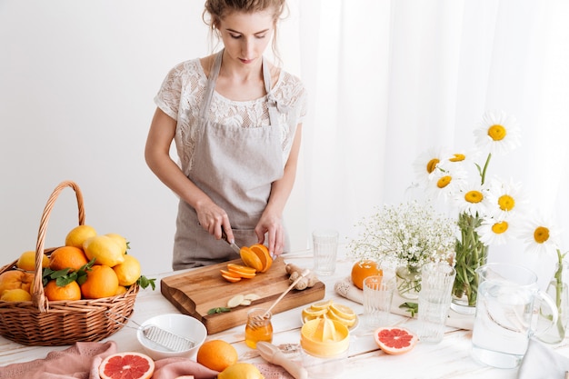 Woman standing indoors cut the orange. Looking aside.