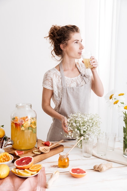 Woman standing indoors drinking citrus beverage