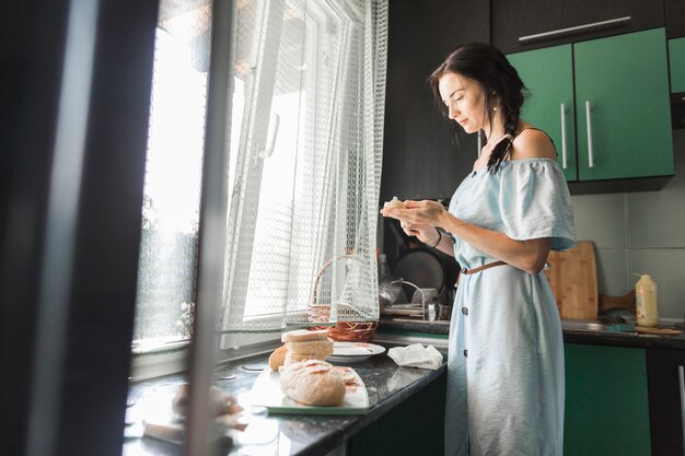 Woman standing in the kitchen applying cheese to bread